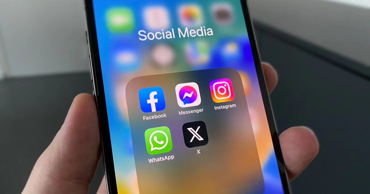 Mano sosteniendo un móvil con la carpeta de aplicaciones de redes sociales
