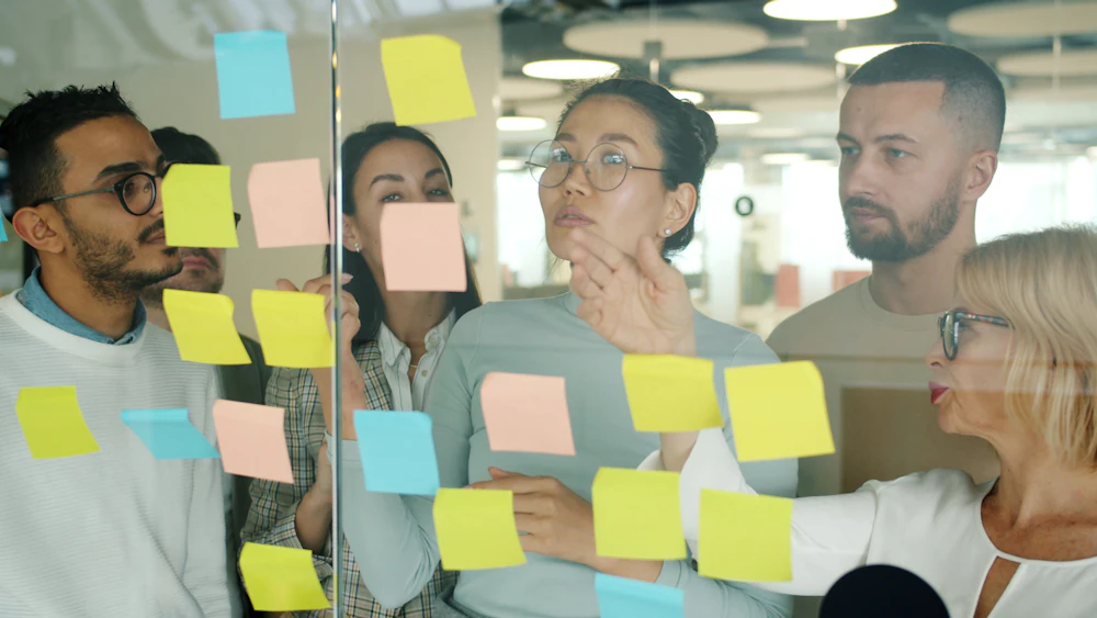 Equipo haciendo una lluvia de ideas con notas adhesivas en una pared de cristal