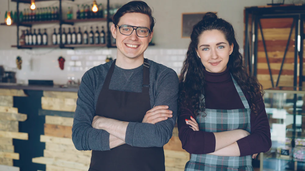 Dos propietarios de una cafetería posando orgullosos en su local